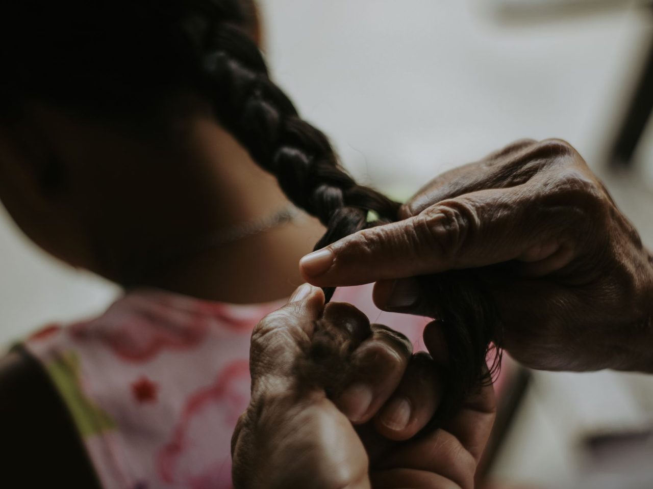 An adult's hands braiding a child's dark hair