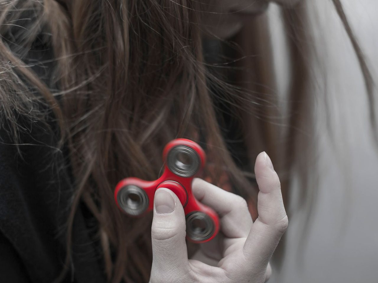 Close-up side view of a woman with long brown hair holding a red three-armed fidget spinner between her fingers.