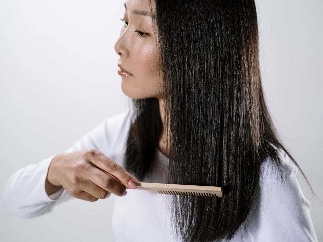 A woman with long straight black hair combing it with a wooden comb